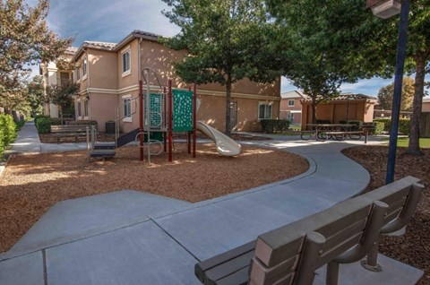 A playground with a slide and a bench in front of a building.